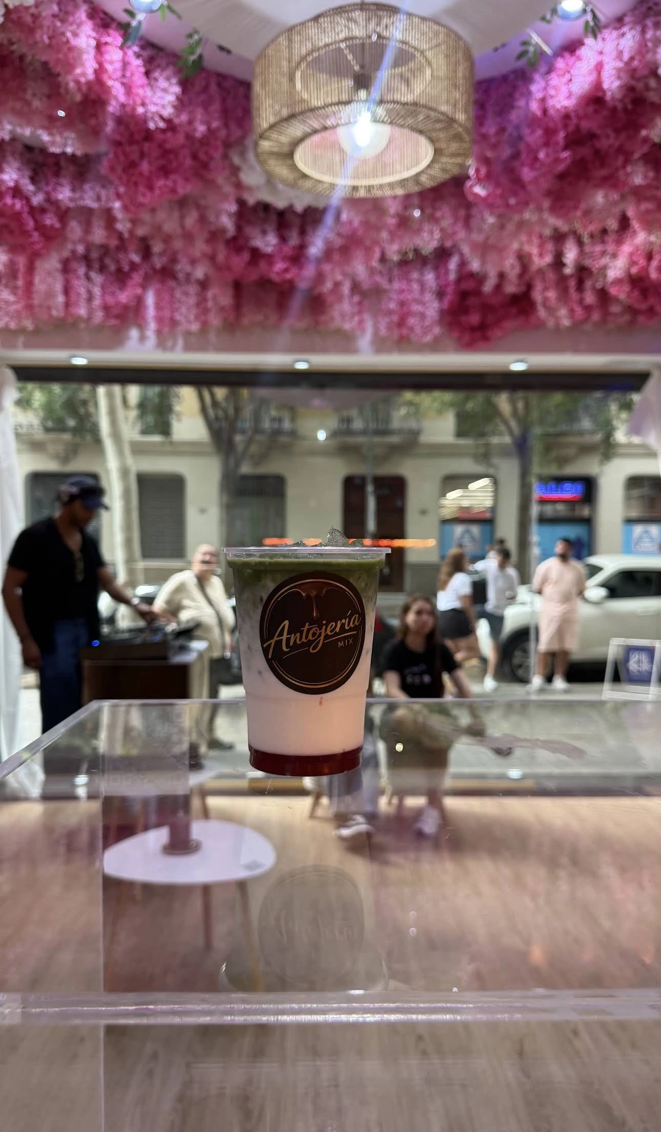 Copa de matcha en la ventana con flores rosas al fondo