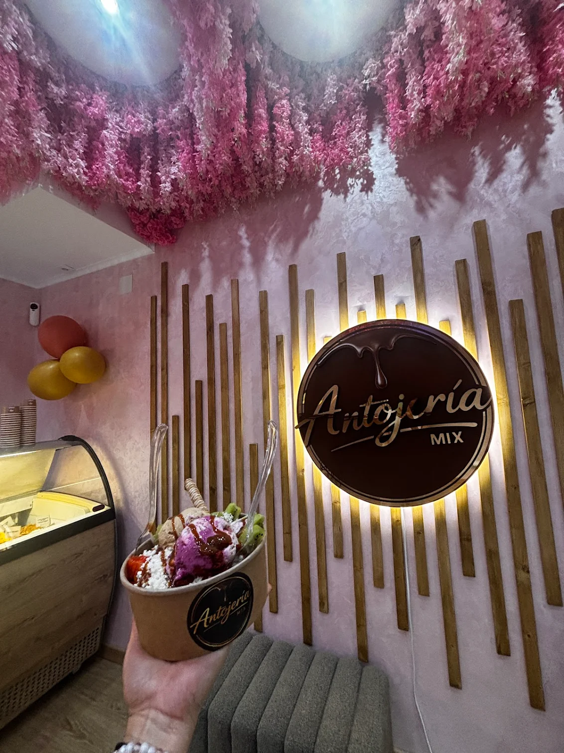Logo iluminado de Antojería Mix con flores rosas en el techo